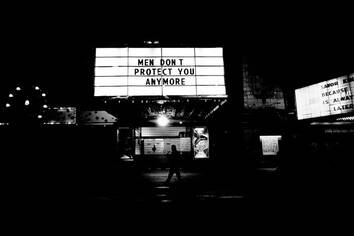 Black and white photograph of a lighted sign that reads "Men Don't Protect You Anymore"